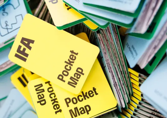 Viele gelbe Faltkarten mit der Aufschrift "IFA Pocket Map" auf einem Stapel.