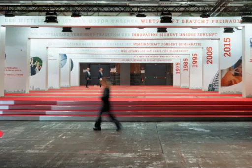 Person geht durch eine modern gestaltete Ausstellungshalle mit roten Stufen und weißen Wänden.