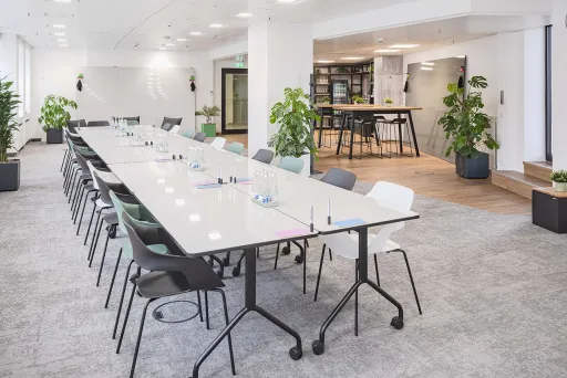 Heller Konferenzraum mit langem Tisch, vielen Stühlen und Pflanzen, moderne Einrichtung.