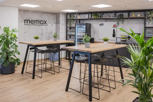 Moderne Büro-Küche mit hohen Tischen, Stühlen und vielen grünen Pflanzen.
