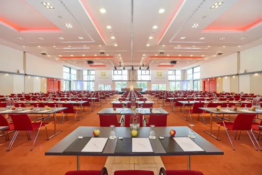 Großer, heller Konferenzsaal mit roten Stühlen und gedeckten Tischen.