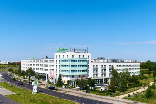 Modernes, weißes Hotelgebäude mit grünem Holiday Inn Logo und umliegender Begrünung.