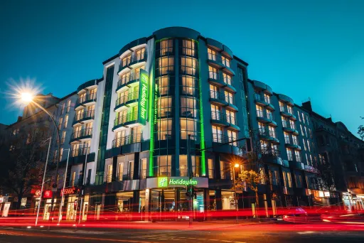 Beleuchtetes Hotelgebäude bei Nacht, vorbeifahrende Autos mit Lichtspuren.