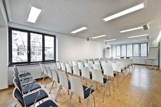 Heller, leerer Konferenzraum mit weißen Stühlen und großen Fenstern.