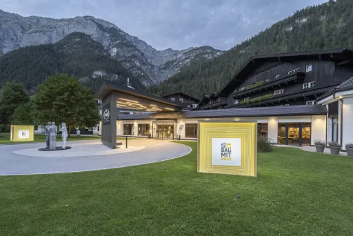 Modernes Gebäude mit Kunstinstallationen im beleuchteten Außenbereich und Bergen im Hintergrund.
