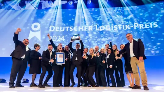 Eine Gruppe steht jubelnd vor einer Leinwand auf der steht: Deutscher Logistik-Preis 2024