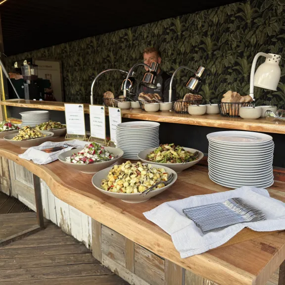 Buffet mit verschiedenen Salaten, gestapelten Tellern und einem Koch im Hintergrund.