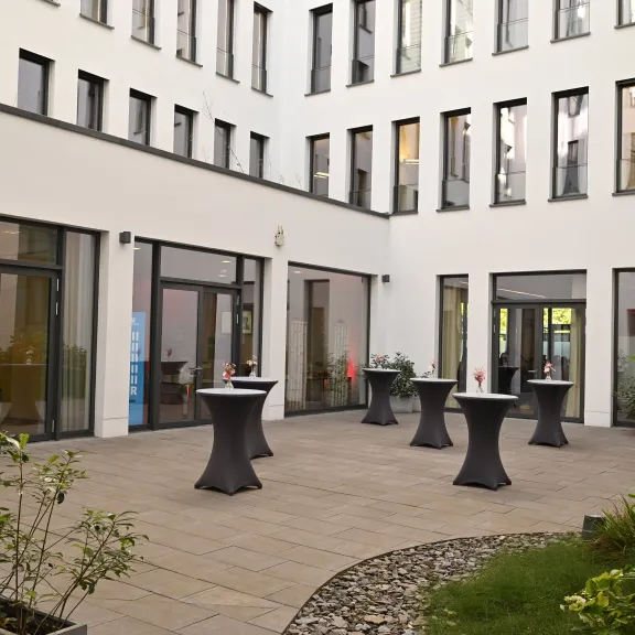 Moderner Innenhof mit Stehtischen, Pflanzen und umliegenden großen Fenstern