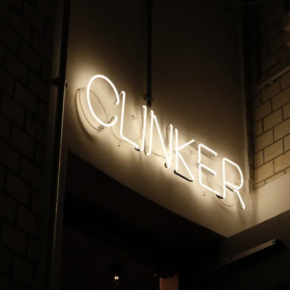 Leuchtreklame mit dem Schriftzug "CLINKER" an einer hellen Ziegelwand bei Nacht.