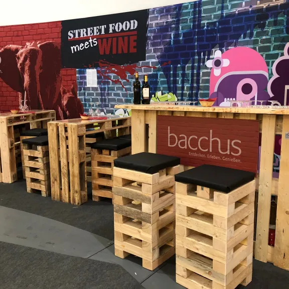 Barbereich aus Holzpaletten mit schwarzer Sitzfläche, bunte Wand mit Street-Food-Graffiti.