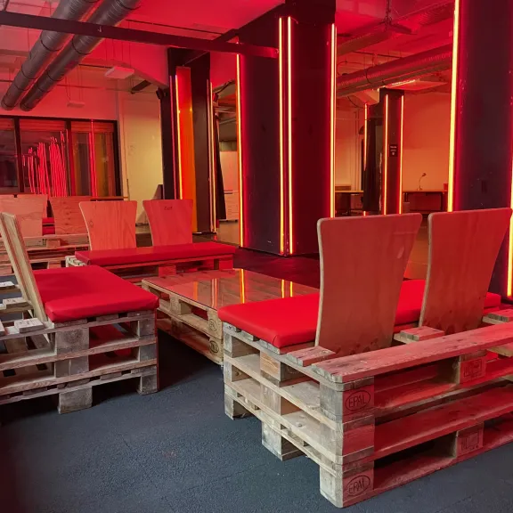 Sitzbereich aus Holzpaletten mit roten Sitzkissen in rot beleuchtetem Raum
