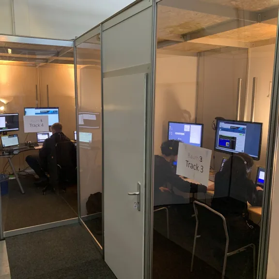 Mehrere Personen arbeiten an Computern in kleinen, abgetrennten Büroräumen.