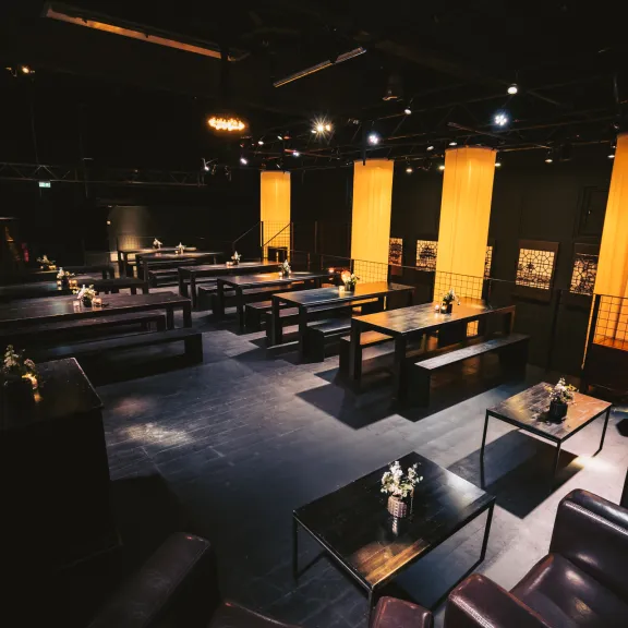 Modernes, dunkel beleuchtetes Lounge-Café mit gelben Lichtsäulen und Ledersofas.