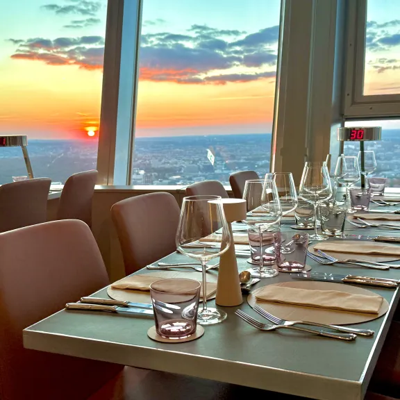 Gedeckter Restauranttisch am Fenster mit Blick auf Sonnenuntergang über der Stadt.