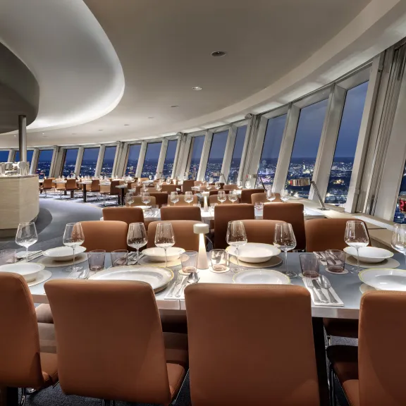 Modernes Restaurant mit gedeckten Tischen und Panoramablick auf die Stadt bei Nacht.