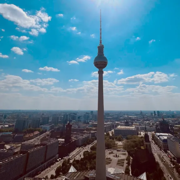 Fernsehturm Berlin vor blauem Himmel und Sonnenstrahlen, Stadt im Hintergrund.