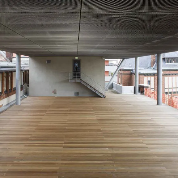 Überdachte Holzterrasse mit Blick auf moderne und historische Gebäude.