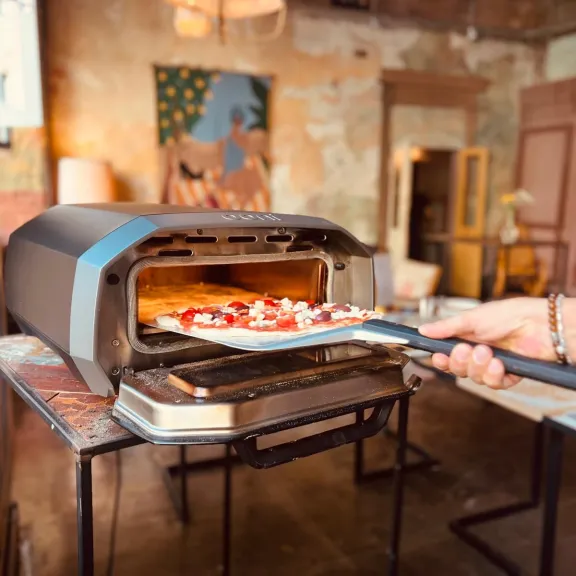 Pizza wird in einen kleinen Ofen in einem gemütlichen Raum geschoben.
