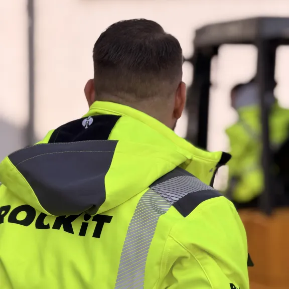 Mann in gelber Warnjacke vor Gabelstapler im Freien