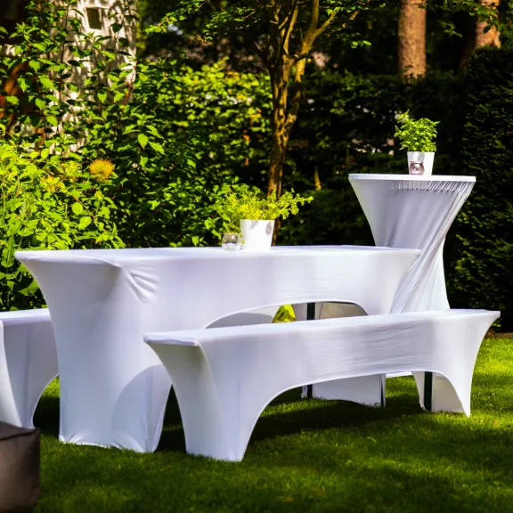 Gedeckter Tisch mit weißen Hussen im Garten, darauf kleine grüne Pflanzen.