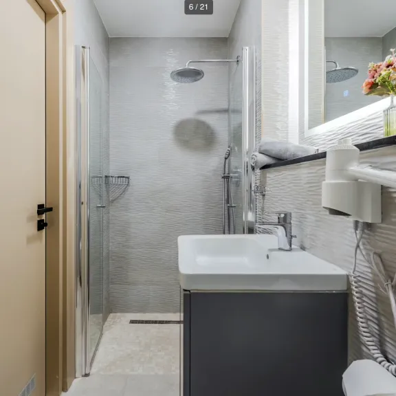 Modernes, schmales Badezimmer mit Dusche, Waschbecken, Spiegel und Föhn an der Wand.
