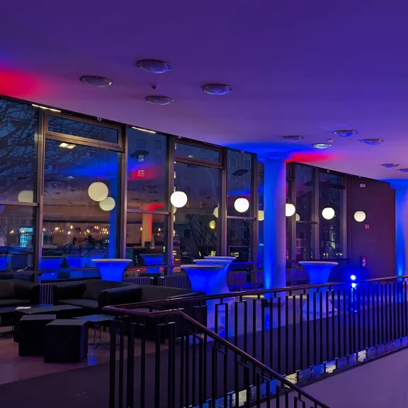 Modernes Foyer mit buntem Licht, runden Lampen und Blick nach draußen bei Abenddämmerung.
