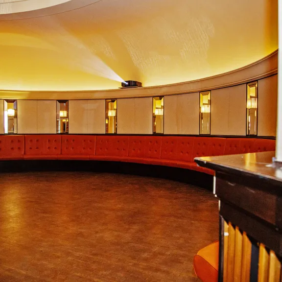 Runder Raum mit orange gepolsterter Sitzbank und warmem Licht.