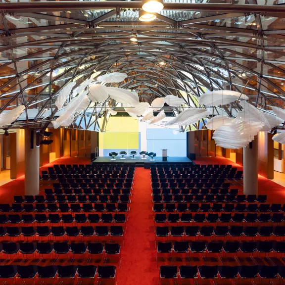 Großer, moderner Konferenzsaal mit roten Stühlen und ungewöhnlicher Deckendekoration.