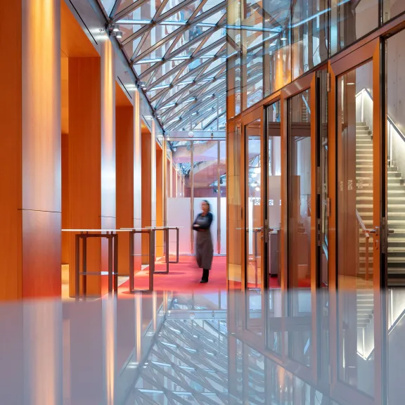 Person steht in modernem, orange erleuchtetem Foyer mit Glasdach und Treppe.