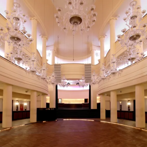 Eleganter Festsaal mit Kronleuchtern, Empore und Parkettboden, warmes Licht.