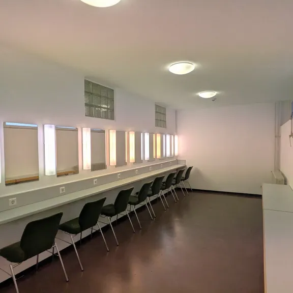Langer, heller Schminkraum mit Spiegeln, Stühlen und weißen Wänden
