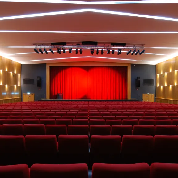 Leerer Theatersaal mit roten Sitzen und rotem Vorhang auf der Bühne