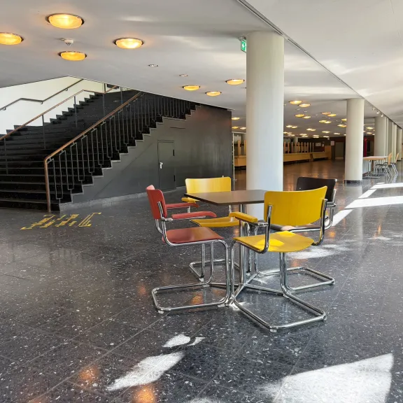 Moderner Flur mit bunten Stühlen, Tisch und Treppe, viel Tageslicht