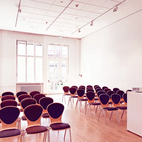 Heller, leerer Konferenzraum mit vielen Stühlen und einem Rednerpult.
