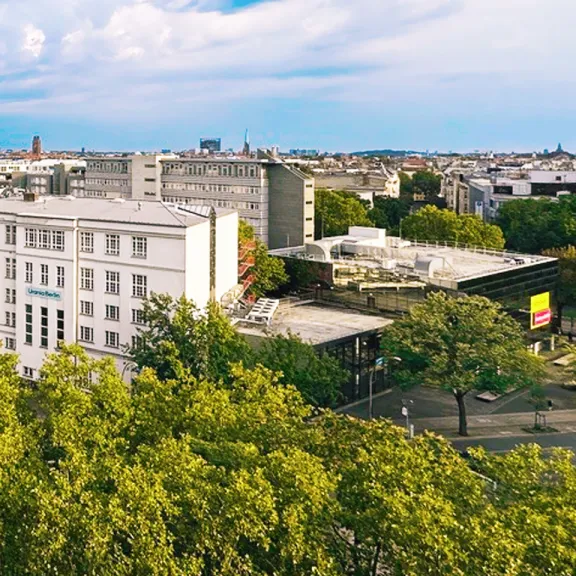 Stadtansicht  der Urania mit grünen Bäumen, weißen und modernen Gebäuden unter blauem Himmel.