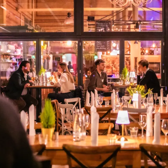 Menschen sitzen in einem gemütlichen, hell erleuchteten Restaurant und unterhalten sich.