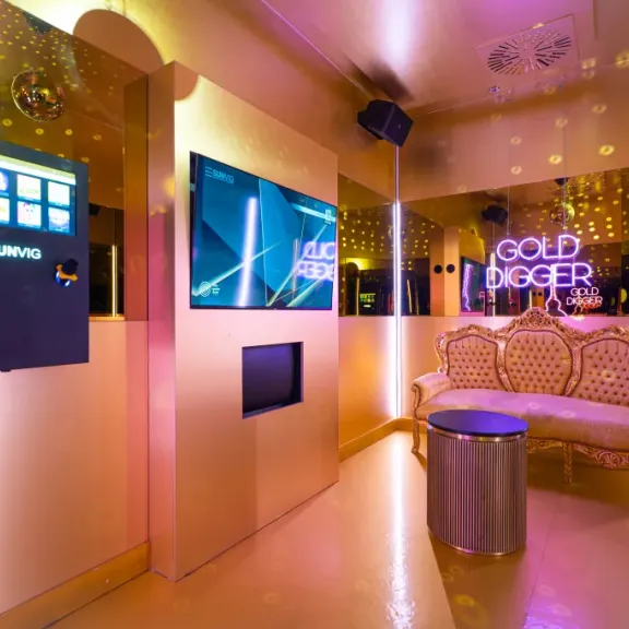 Goldener Raum mit luxuriösem Sofa, Spiegeln, Automaten und bunter Beleuchtung.