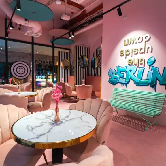 Modernes Café mit rosa Wänden, Marmortischen und Neon-Schriftzug „Berlin“ an der Wand.
