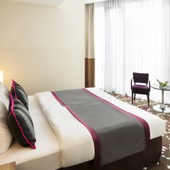 Modernes Hotelzimmer mit Doppelbett, zwei Stühlen und bodentiefen Fenstern.