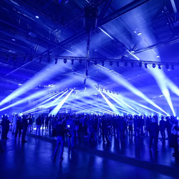 Menschenmenge in Halle, blaue Lichter und Strahler erzeugen Festivalstimmung