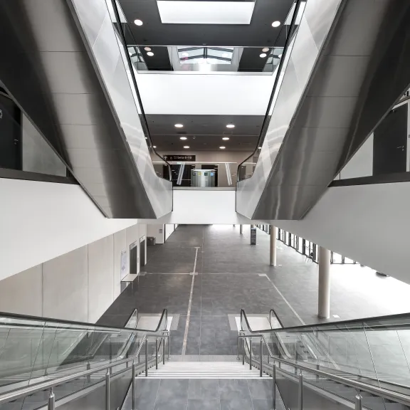 Breite Treppe mit Glasgeländer in modernem, hellen Gebäude mit Oberlicht.