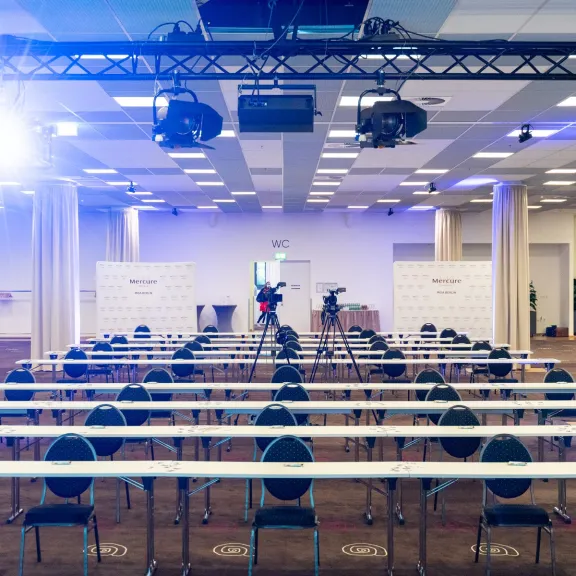 Leerer Konferenzraum mit Reihenstühlen, Bühne und Kameraleuten.