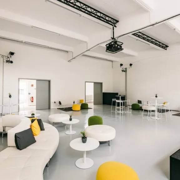 Heller, moderner Lounge-Bereich mit weißen Sofas, gelben Hockern und kleinen Tischen.