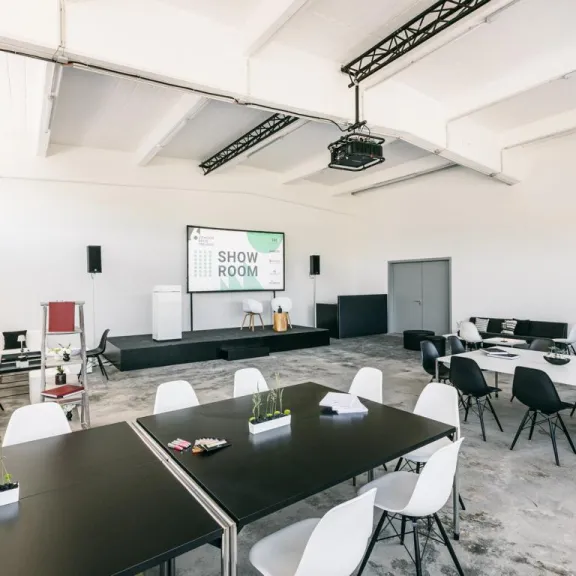 Heller Seminarraum mit Tischen, Stühlen und großer Präsentationsleinwand.