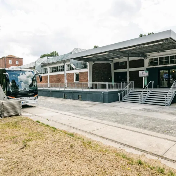 Reisebus vor modernem Backsteingebäude mit Rampe und Treppe, bewölkter Himmel