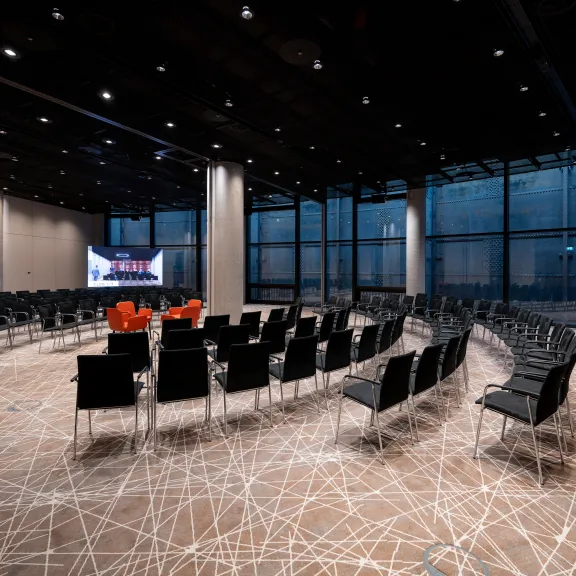 Moderner Konferenzraum mit schwarzen Stühlen im Halbkreis und zwei großen Bildschirmen.