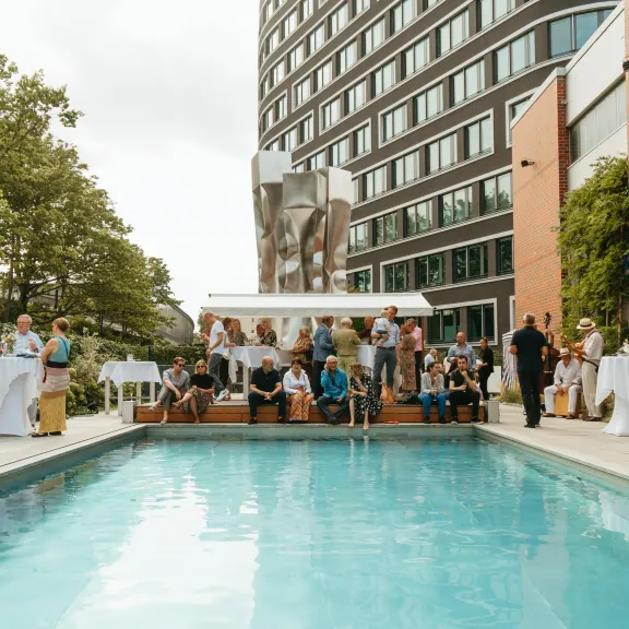 Menschen feiern entspannt an einem Pool neben einem modernen Gebäude.