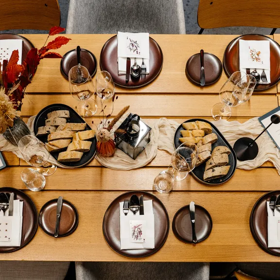 Festlich gedeckter Holztisch mit Tellern, Gläsern, Trockenblumen und Snacks.