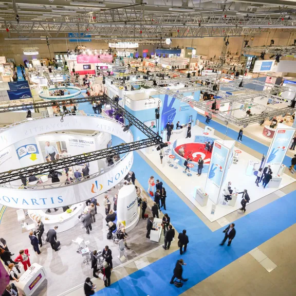 Fotografie einer großen Messehalle mit zahlreichen Ständen und vielen Besuchern.