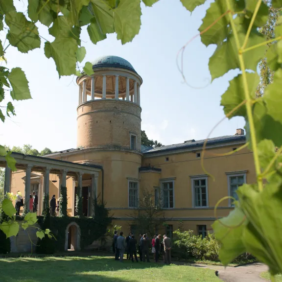 Yellow observatory building framed by green leaves, people gathered near the entrance.